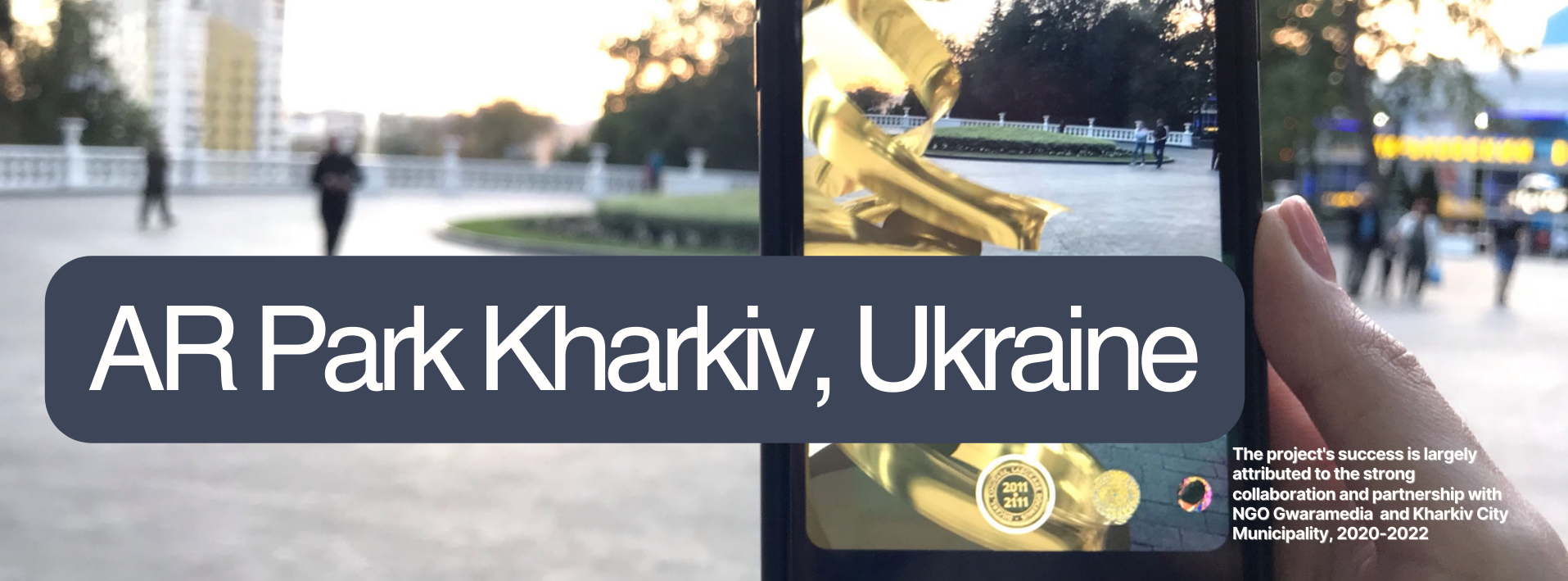 View of the AR Calligraffiti Sculpture Park in Kharkiv, Ukraine, showcasing an augmented reality sculpture on a smartphone screen held by a visitor.